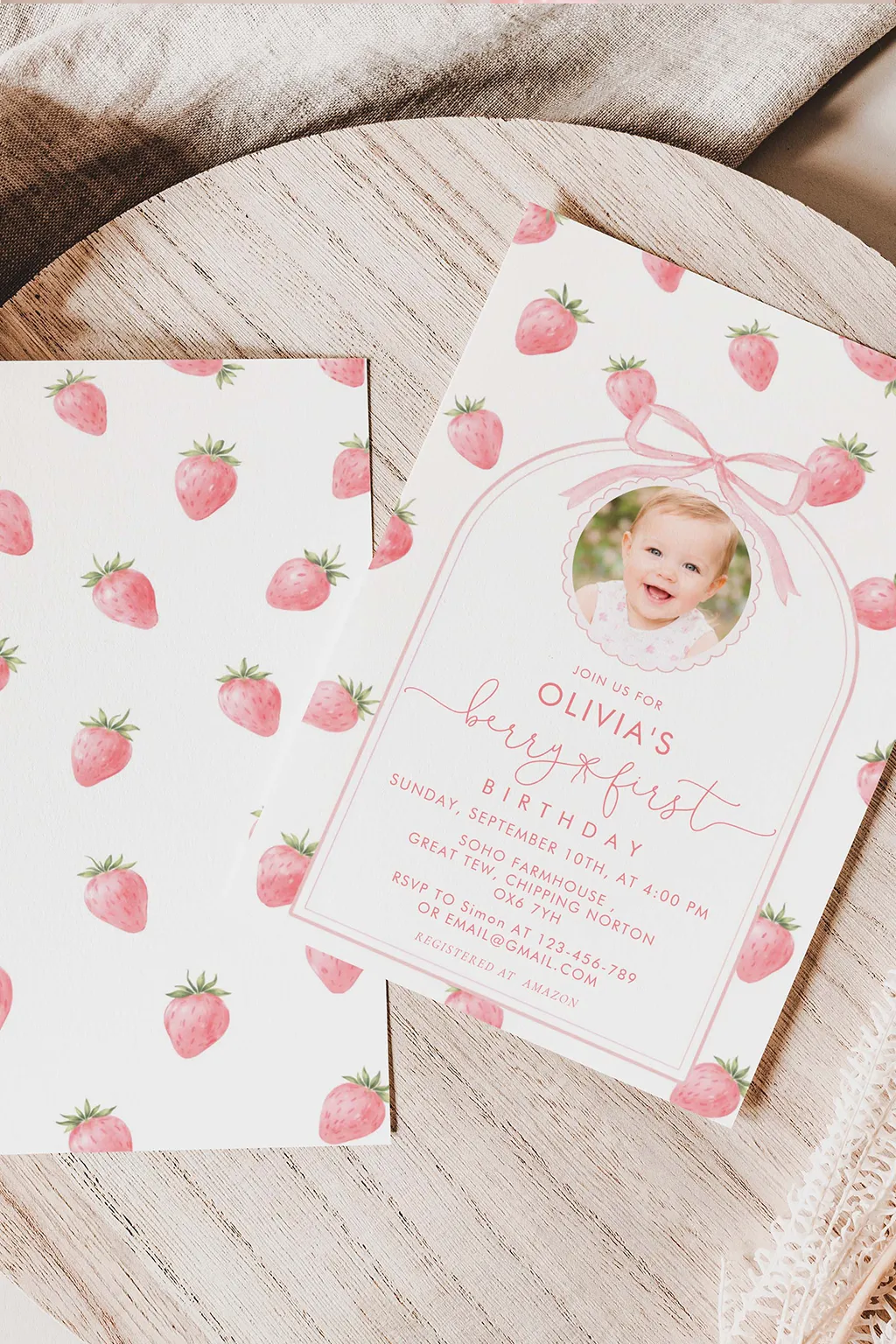 Berry first birthday invitation flat lay — watercolor strawberries, a little bow and soft pink